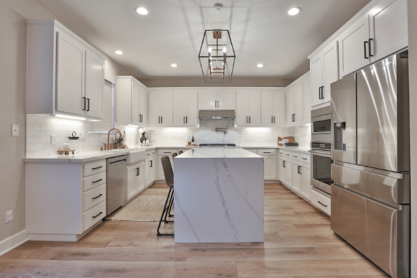 View of marble island with stainless steel fridge and white cabinets. 