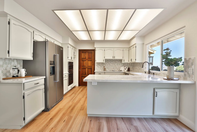 light wood floors with white cabinets and counters. a unique wood panel door and paneled lights. 