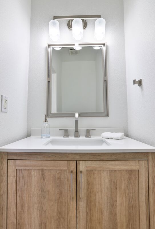 silver hardware mirror and sink with a white top counter and white walls.
