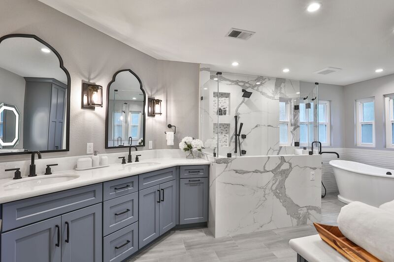 Blue cabinets and grey hardwood floor with two half square, curved top mirrors and a white bath.