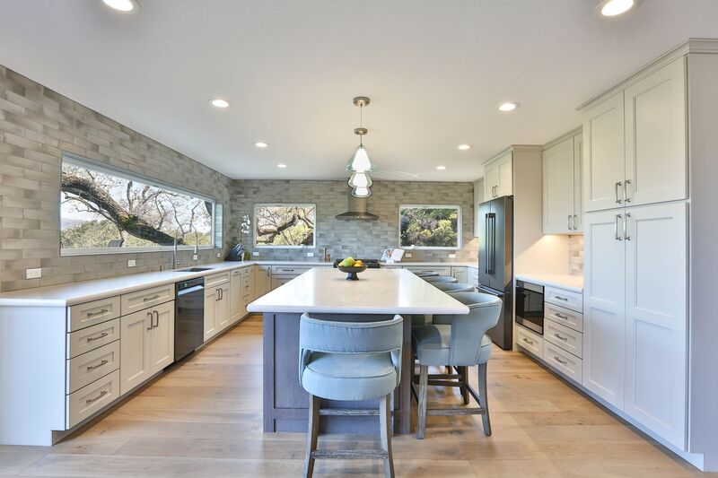 Kitchen with island, hardwood floors, and white cabinets, with grey rectangle tile. 