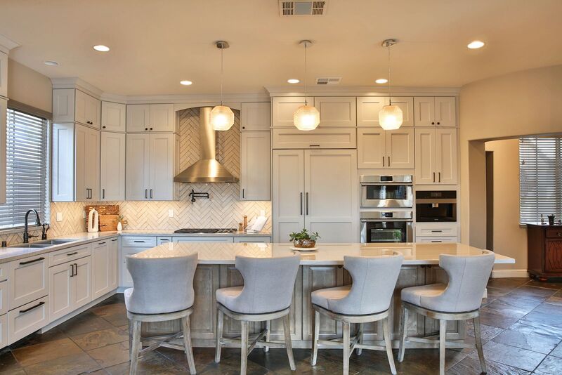 Four white chairs facing a white counter island in a white cabinet kitchen