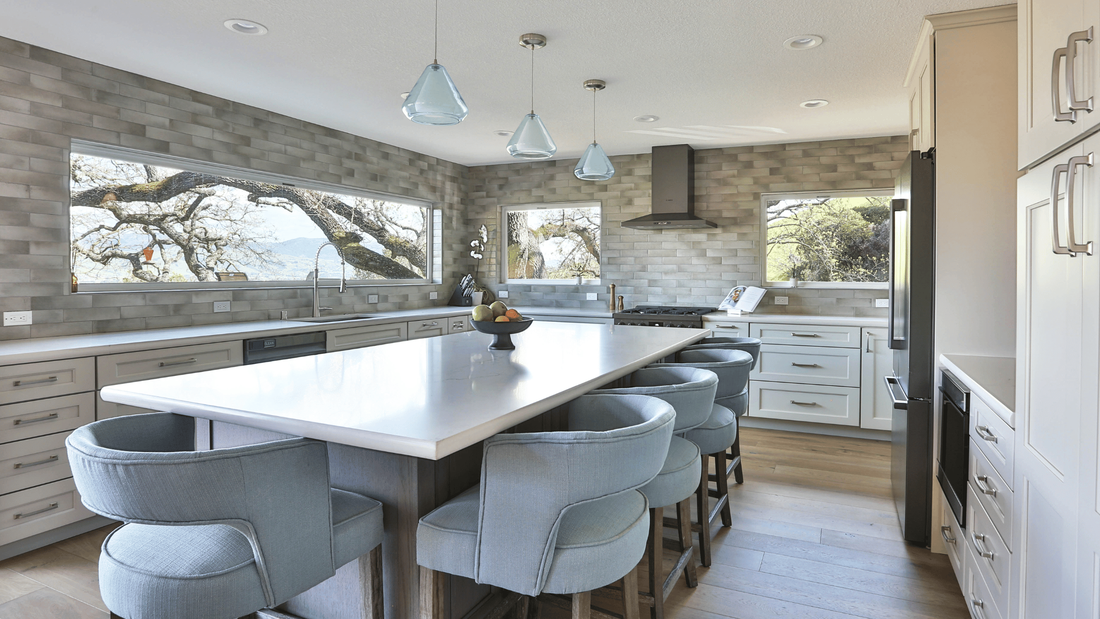 newly designed kitchen with gray gradient glazed tile, off-white cabinets, and pale blue upholstered stools around a large kitchen island