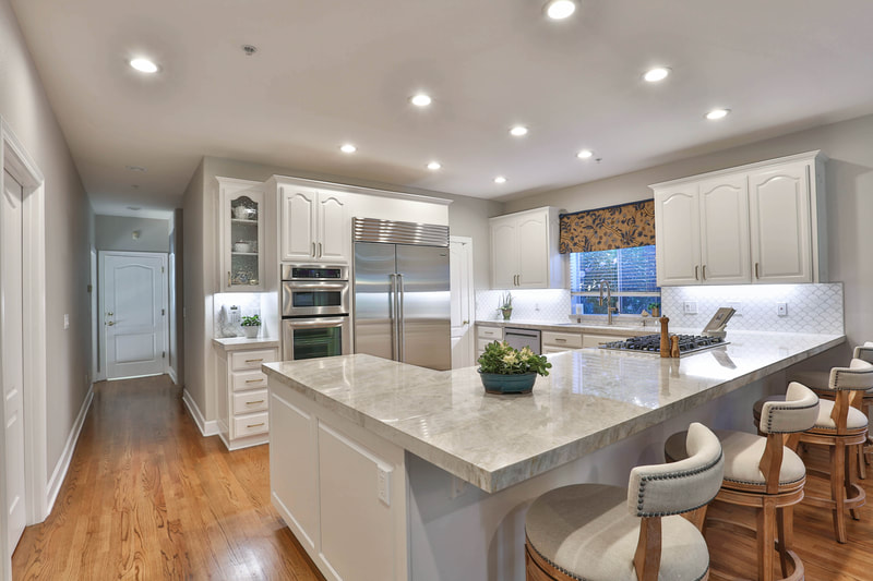 angled view of white marbled countertop with white cabinets and hardwood floor