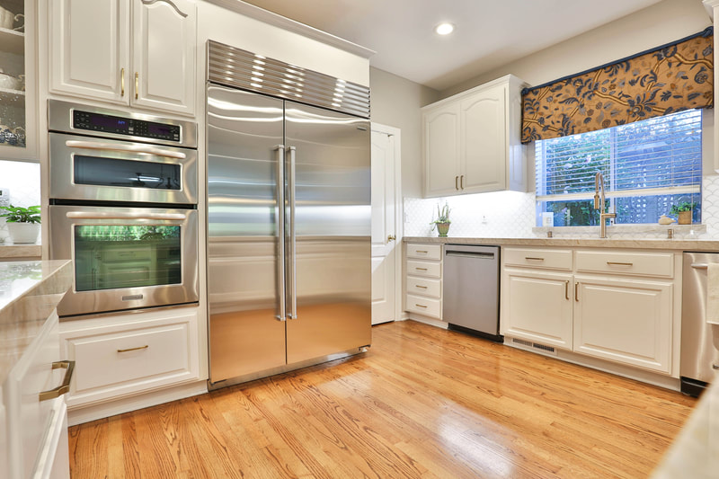 View of refrigerator in kitchen with white cabinets and wood floors